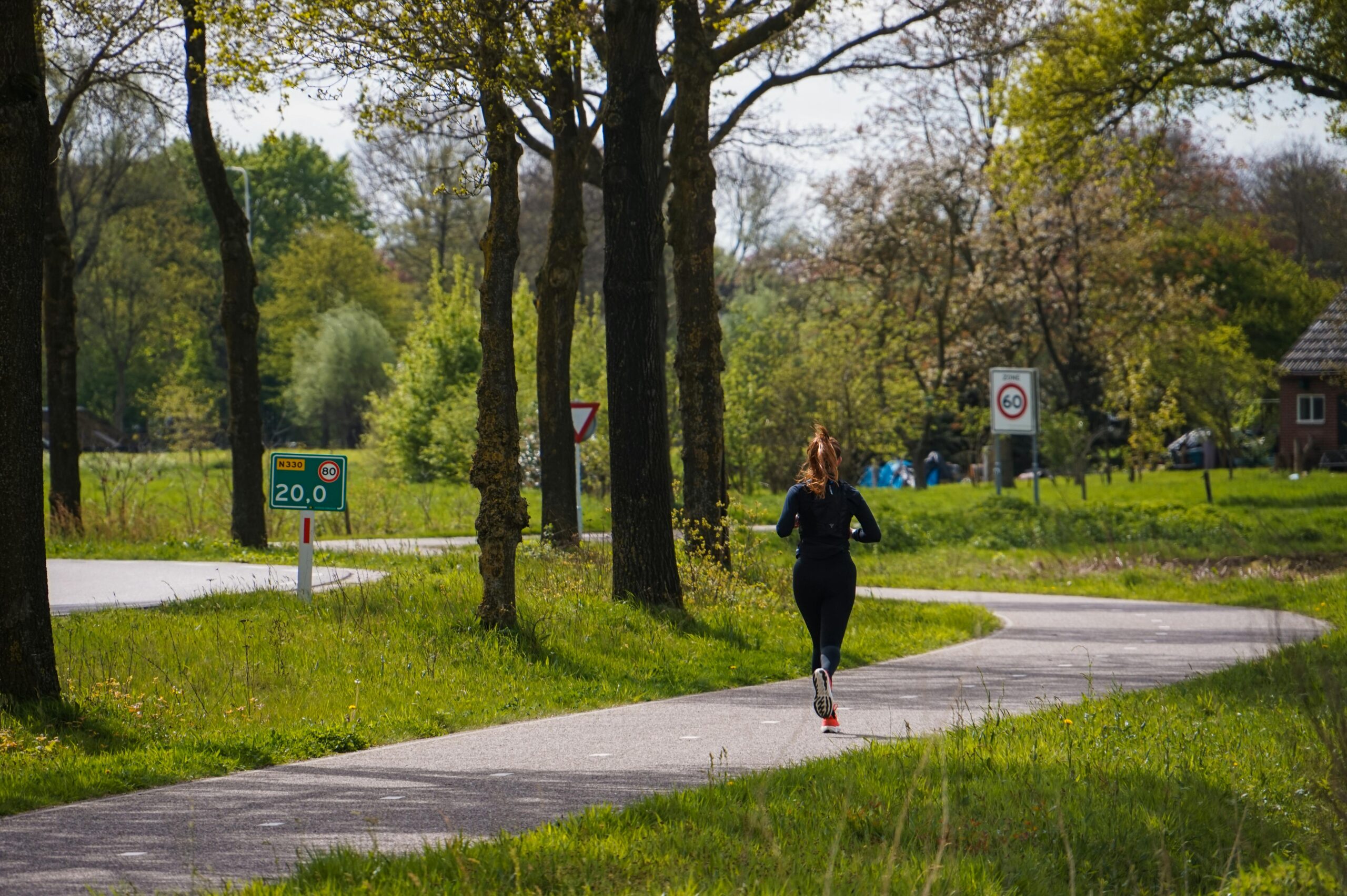 A woman runs along a winding path in a lush, green forest in springtime, enjoying the serene natural setting.